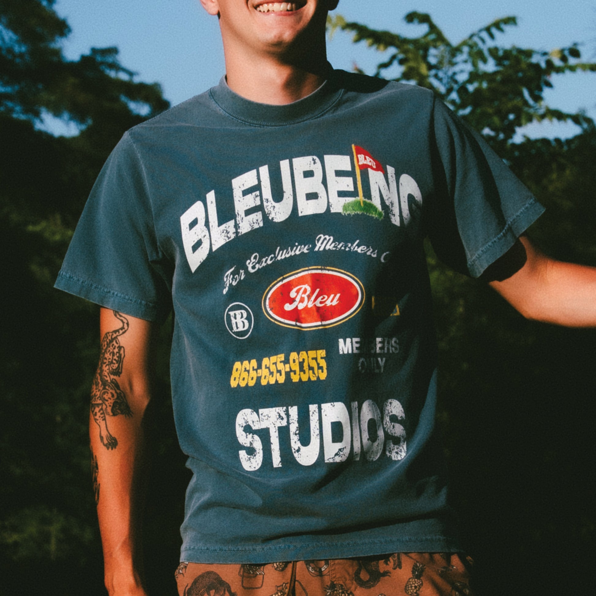 front view of model wearing slate blue bleubeing studios graphic t shirt with bold print on front with sky background.